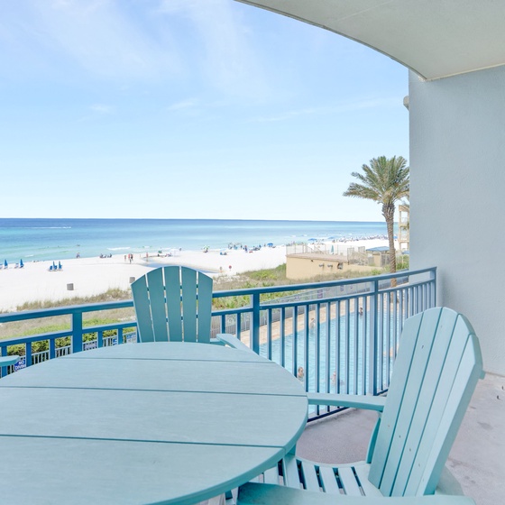 Savor morning coffee on your private balcony with stunning beach views, watching the turquoise waters while enjoying the comfortable outdoor dining setup.