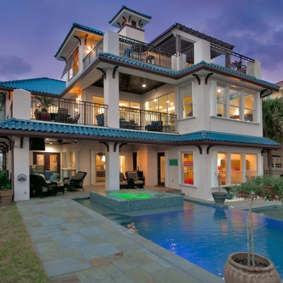 Elegant coastal villa features distinctive blue-tile roofing and multi-level architecture, complemented by tropical landscaping and neighboring properties in this desirable area.
