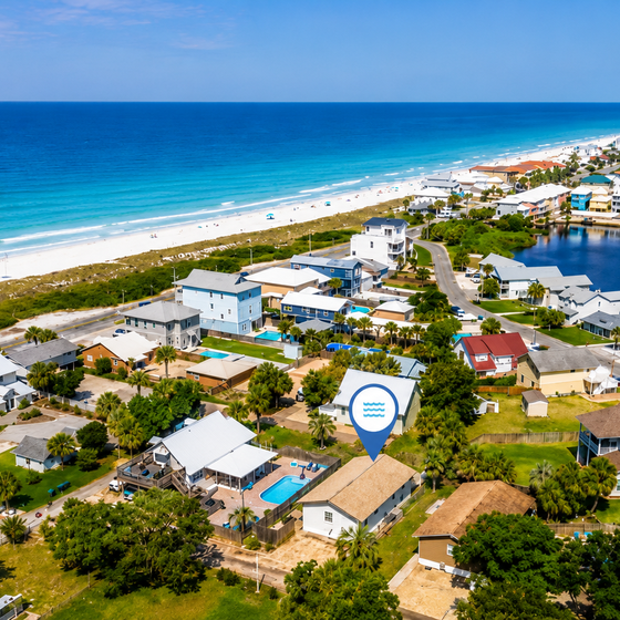Aerial view of a beachfront coastal community with palm trees, residential properties, and a tranquil inland waterway alongside pristine sandy shores and turquoise ocean waters.