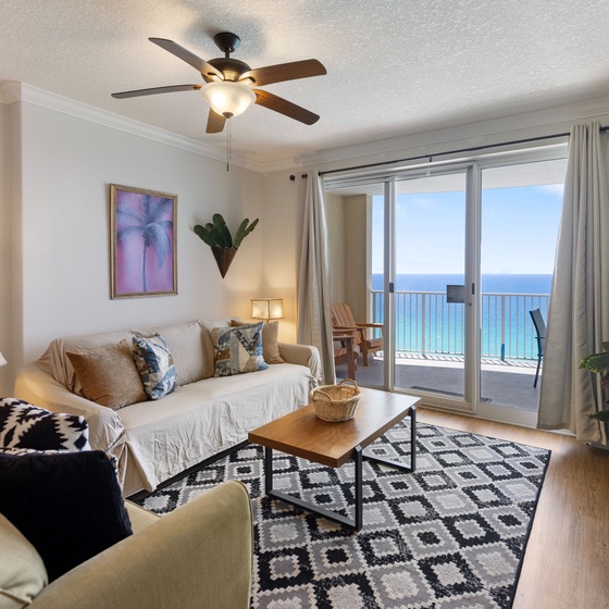 Relax in your bright living space with stunning ocean views through floor-to-ceiling windows, complete with cozy seating and modern amenities.