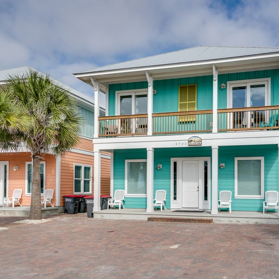 Charming turquoise beach house with tropical palms and front porch seating for the perfect coastal getaway.