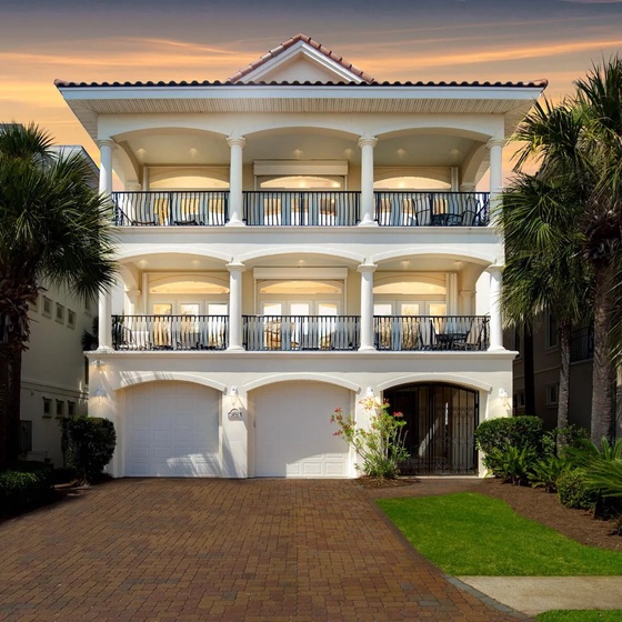 Elegant three-story vacation home with spacious balconies and tropical palm landscaping welcomes guests at arrival.