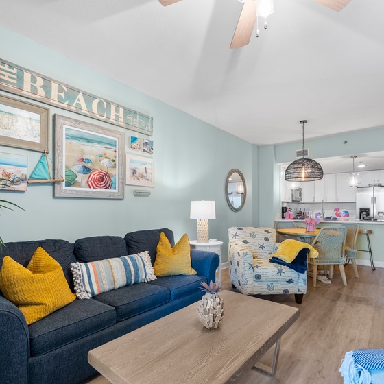Relax in your coastal-themed living space with beach artwork, comfortable seating, and an open kitchen perfect for vacation dining.