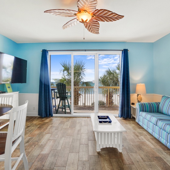 Relax in your bright coastal living room with stunning balcony views of swaying palms and blue skies.