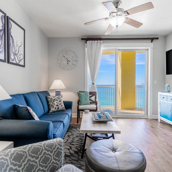 Your coastal living room opens to stunning ocean views through glass doors, with nautical decor and comfortable seating for perfect beach relaxation.