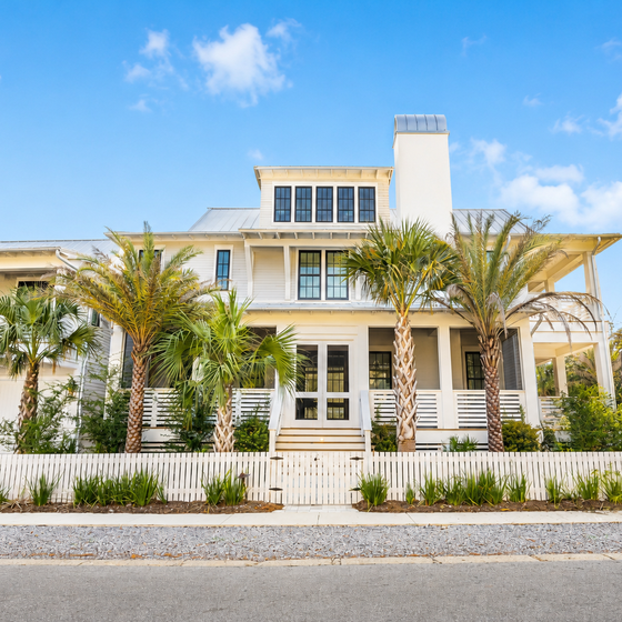 Stunning coastal home with elegant white facade, palm-lined entrance, and modern architectural details in a peaceful residential setting.