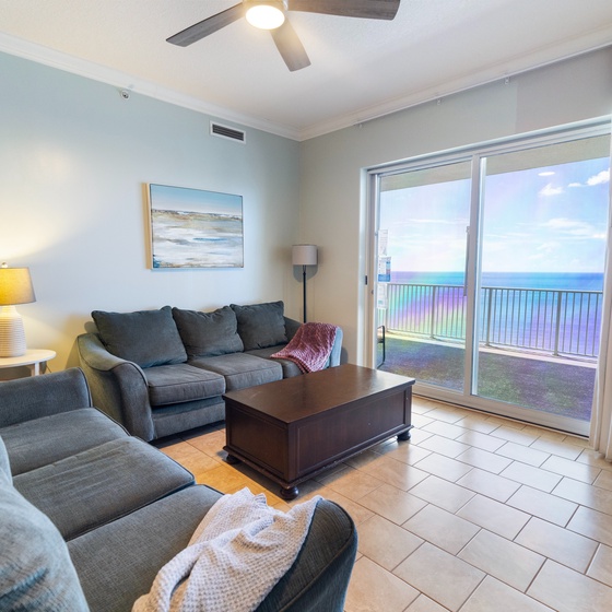 Sink into plush coastal comfort while gazing at the stunning ocean through your private balcony doors. This inviting living room blends soft blues and grays, offering a tranquil space to unwind after sun-soaked beach days.