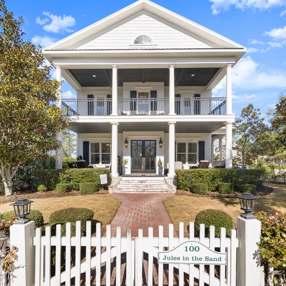 Charming Southern-style home with classic white columns and wraparound porches, nestled among mature trees in a peaceful neighborhood setting.