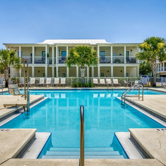 Property features a central swimming pool surrounded by tropical palm trees and multi-story vacation rental buildings with balconies.