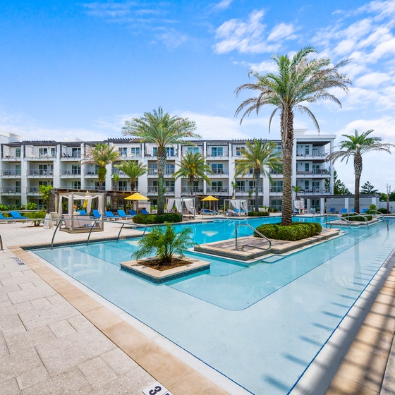 Modern resort-style pool area with palm trees and contemporary buildings.