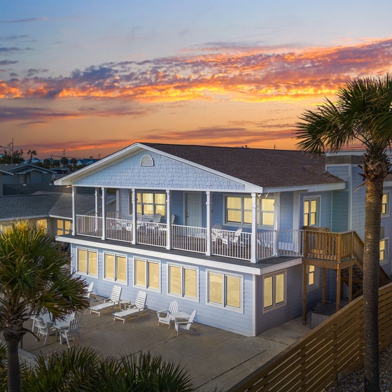 This coastal property showcases a stunning two-story beach house with expansive balconies surrounded by swaying palm trees during golden hour.