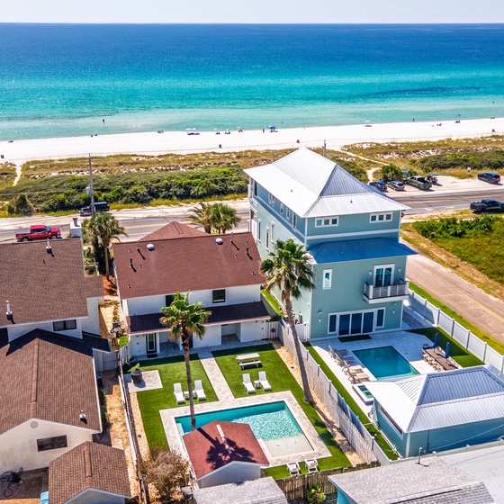 Aerial view of beachfront vacation rentals with private pools, just steps from pristine white sand and turquoise Gulf waters. The property offers convenient beach access across the coast road.