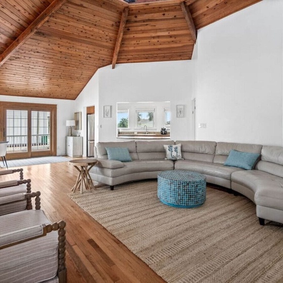 Unwind in this stunning open-concept living space where coastal charm meets rustic elegance beneath soaring wood-beamed ceilings.