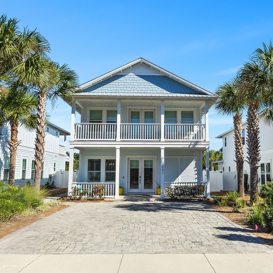 A charming two-story coastal home with traditional balconies and tropical palm trees, perfectly positioned in a peaceful beachside neighborhood.