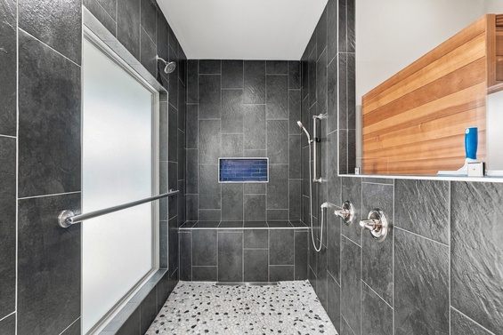 Step into your beautifully designed walk-in shower with modern slate-gray tiles and double showerheads for a refreshing rinse after a day exploring the area.