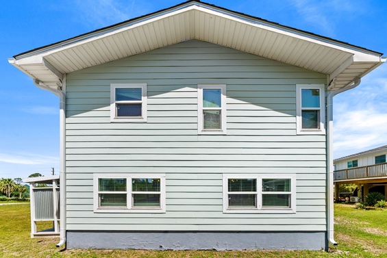 This two-story coastal home features clean white siding, a spacious design, and a welcoming front façade surrounded by an open lawn and neighboring properties.