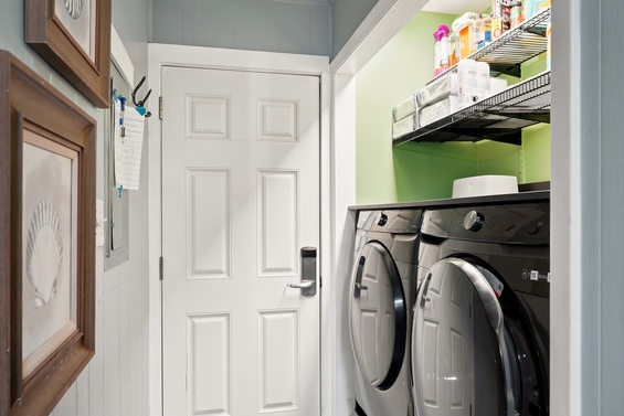 A full-sized washer and dryer await you in this neatly organized laundry area, complete with shelving for supplies and a cheerful pop of green.