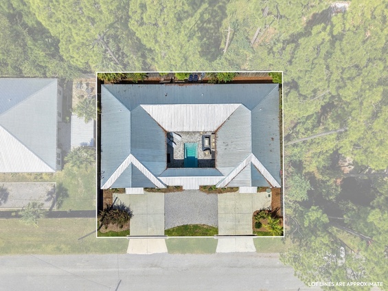 An aerial view of the property nestled among lush greenery, showcasing the metal roof, private pool area, and spacious lot surrounded by natural landscape.