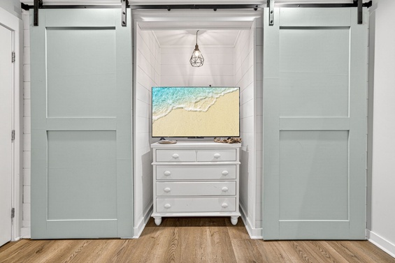 Slide open the charming barn doors to reveal your cozy bedroom nook with a wall-mounted TV and dresser—your perfect coastal retreat.
