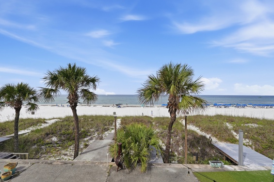 Beachfront property featuring white sandy shores, swaying palm trees, and a wooden boardwalk leading to the water, with calm ocean waters stretching to the horizon.