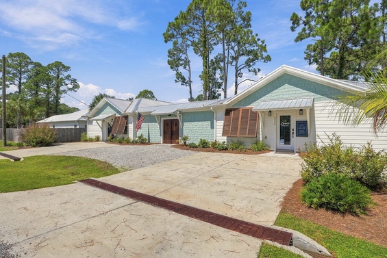 A charming coastal-style cottage nestled among towering pines, where fresh landscaping and a welcoming front entrance set the tone for a relaxing getaway.
