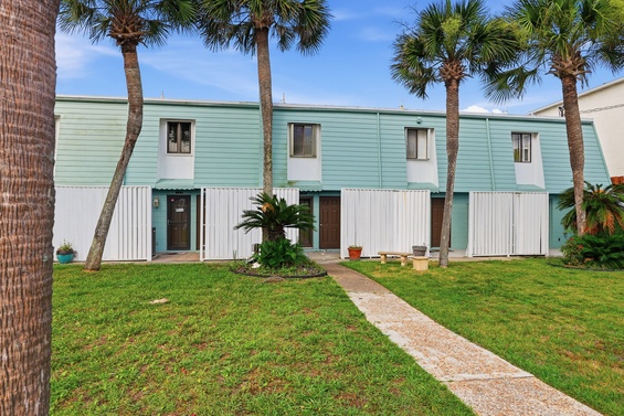 A charming beach-style property framed by swaying palms and lush greenery, offering a peaceful coastal retreat under sunny blue skies.