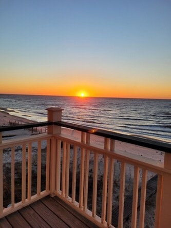 Stunning beachfront sunset paints the horizon in golden hues, visible from the property's waterfront balcony overlooking the serene coastline.