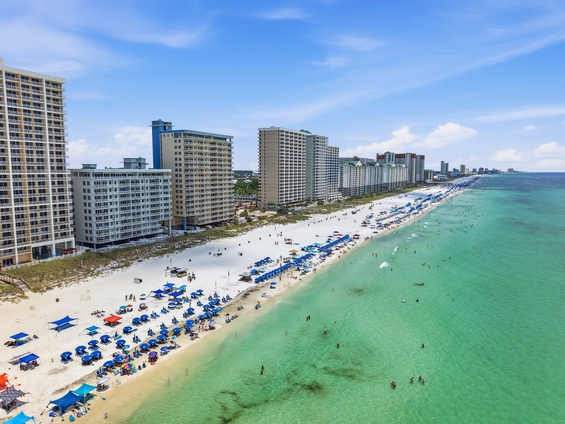 An aerial view of the beachfront location, featuring white sand, turquoise waters, and a stretch of high-rise buildings lining the coast near the property.