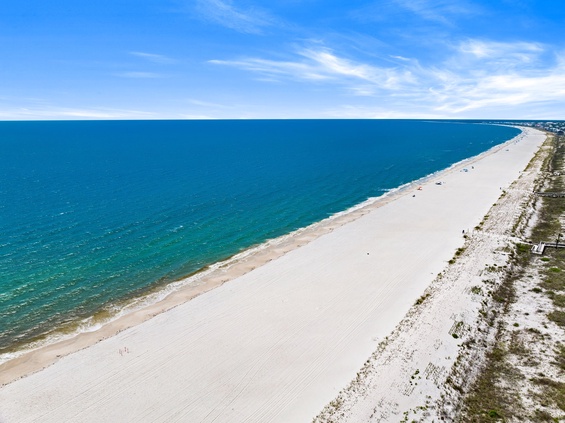 A stunning bird's-eye view captures miles of pristine white sand beach stretching along turquoise waters under a bright blue sky—showcasing the serene coastal setting.
