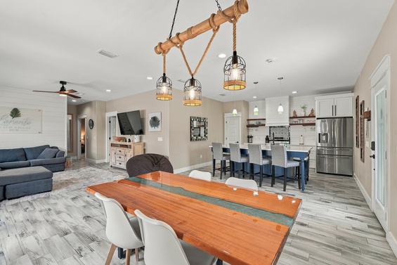 Gather around the rustic wood table under charming nautical lighting for morning coffee or game night laughter. The open dining and kitchen layout creates the perfect backdrop for quality time together.
