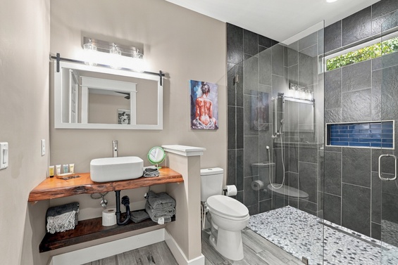 Step into your modern retreat where sleek dark tiles and a glass-enclosed shower await your refreshing morning ritual, while natural light fills the space through a tranquil garden view.