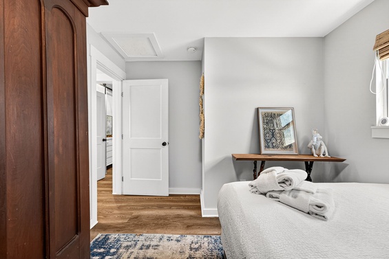 Your serene bedroom sanctuary awaits, featuring a plush bed with fresh towels, warm hardwood floors, and tasteful decor that invites you to settle in and truly relax.