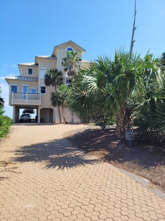 This coastal home features secure covered parking and mature palm trees framing a welcoming brick-paver driveway, located near the beach in a warm-climate neighborhood.