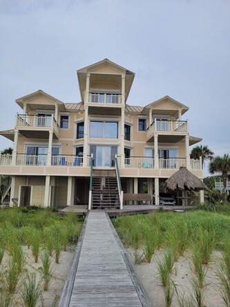Beachfront property with direct access via wooden walkway, featuring multiple levels and balconies overlooking the ocean. Perfect coastal escape with easy beach access.