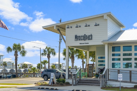 Mexico Beach Welcome Center marks the coastal community's entrance, featuring white coastal architecture amid swaying palms and blue skies along the Gulf Coast.