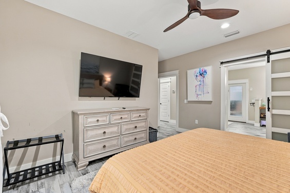 Relax in your serene bedroom with soft neutral tones, a cozy bed dressed in golden-hued linens, and modern touches like the stylish ceiling fan and sleek barn door leading to your private ensuite.