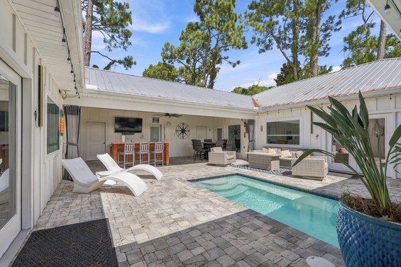 Step into your private courtyard oasis, where a sparkling pool awaits beneath tall pines, surrounded by comfortable loungers and inviting outdoor seating.