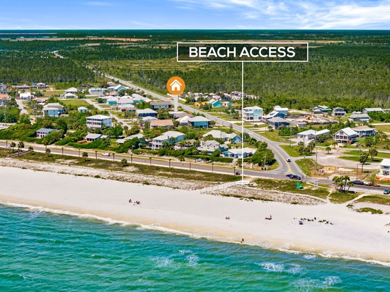 Aerial view of a beachfront neighborhood with direct access to pristine white sand beaches and turquoise waters, surrounded by lush natural landscapes.
