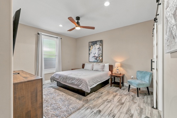 Slip into soft sheets under gentle fan breezes in your calming bedroom retreat, where warm lighting and a cozy chair invite you to unwind completely.