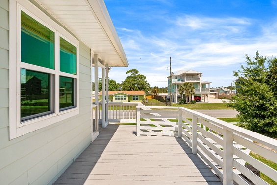 A sunny coastal neighborhood welcomes you, visible from this covered ramp with white railings offering glimpses of nearby homes and greenery under a blue sky.