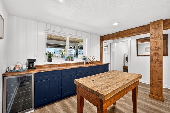 Your coastal kitchen blends rustic wood beams and rich navy cabinetry with modern touches. Sunlight streams through the window, highlighting the handcrafted wood island—perfect for morning coffee or meal prep.