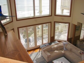 A dramatic two-story living space where natural light pours through floor-to-ceiling windows, framing your deck views. Cozy seating invites you to relax in this airy retreat.
