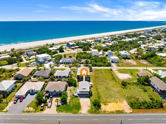 Aerial view of a coastal vacation rental community with pristine beachfront access, surrounded by lush greenery and stunning turquoise waters stretching to the horizon.