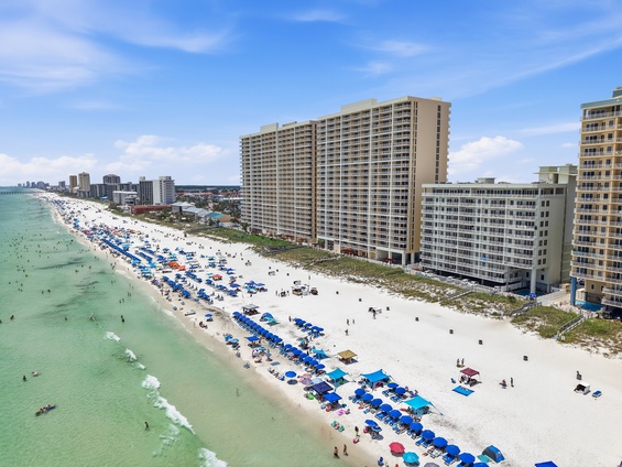 Aerial view of the beachfront property and surrounding coastal area, showcasing the pristine white sand beach and turquoise Gulf waters just steps away from the building.