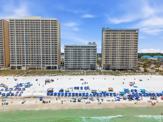 Beachfront high-rise resort complex with direct beach access, rental chairs and umbrellas, and calm turquoise waters along a pristine sandy shore.