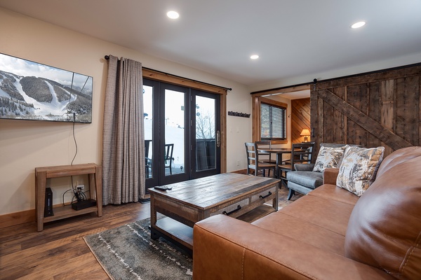 Relax in your inviting living space with rich leather seating, rustic wood accents, and mountain views streaming through the glass doors to your private patio.