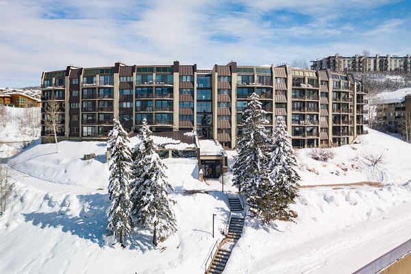 A modern mountain property set in a pristine winter landscape with snow-dusted evergreens and ski-in access, surrounded by neighboring resorts and hillside vistas.