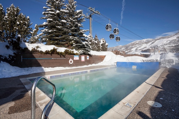 Heated outdoor pool nestled in a snowy mountain resort, surrounded by alpine trees and gondolas overhead—a tranquil spot after a day on the slopes.