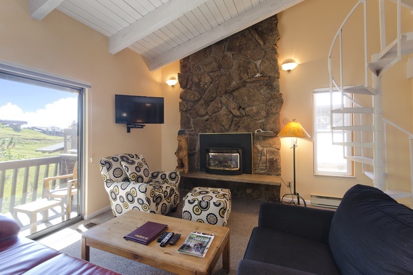 Relax in your cozy living room with vaulted ceilings, a striking stone fireplace, and sweeping views of rolling hills from your private balcony.