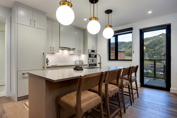 Your modern kitchen glows with natural light, where a spacious island with seating invites casual meals while you take in stunning mountain vistas through large glass doors.